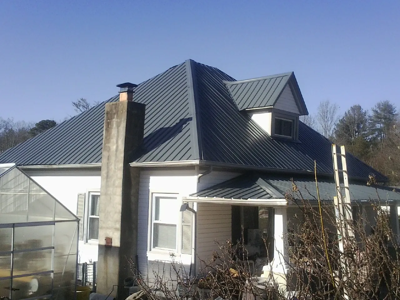 Dark blue standing seam metal roof on a white farmhouse with dormer — Slate & Tile Roof Repair by Roofing Brothers in Green Isle