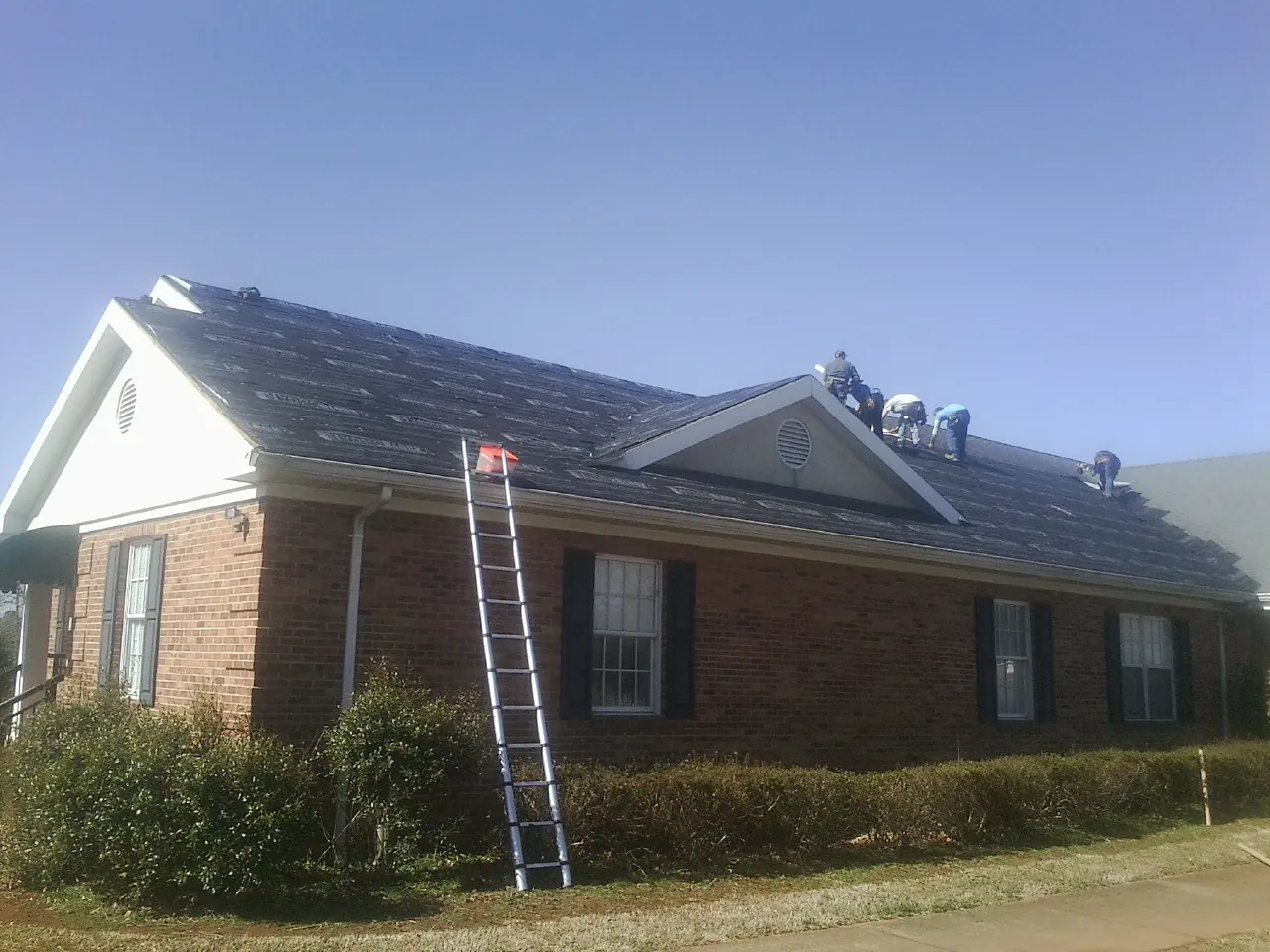 Crew tearing shingles off a brick ranch roof with a ladder set in Green Isle