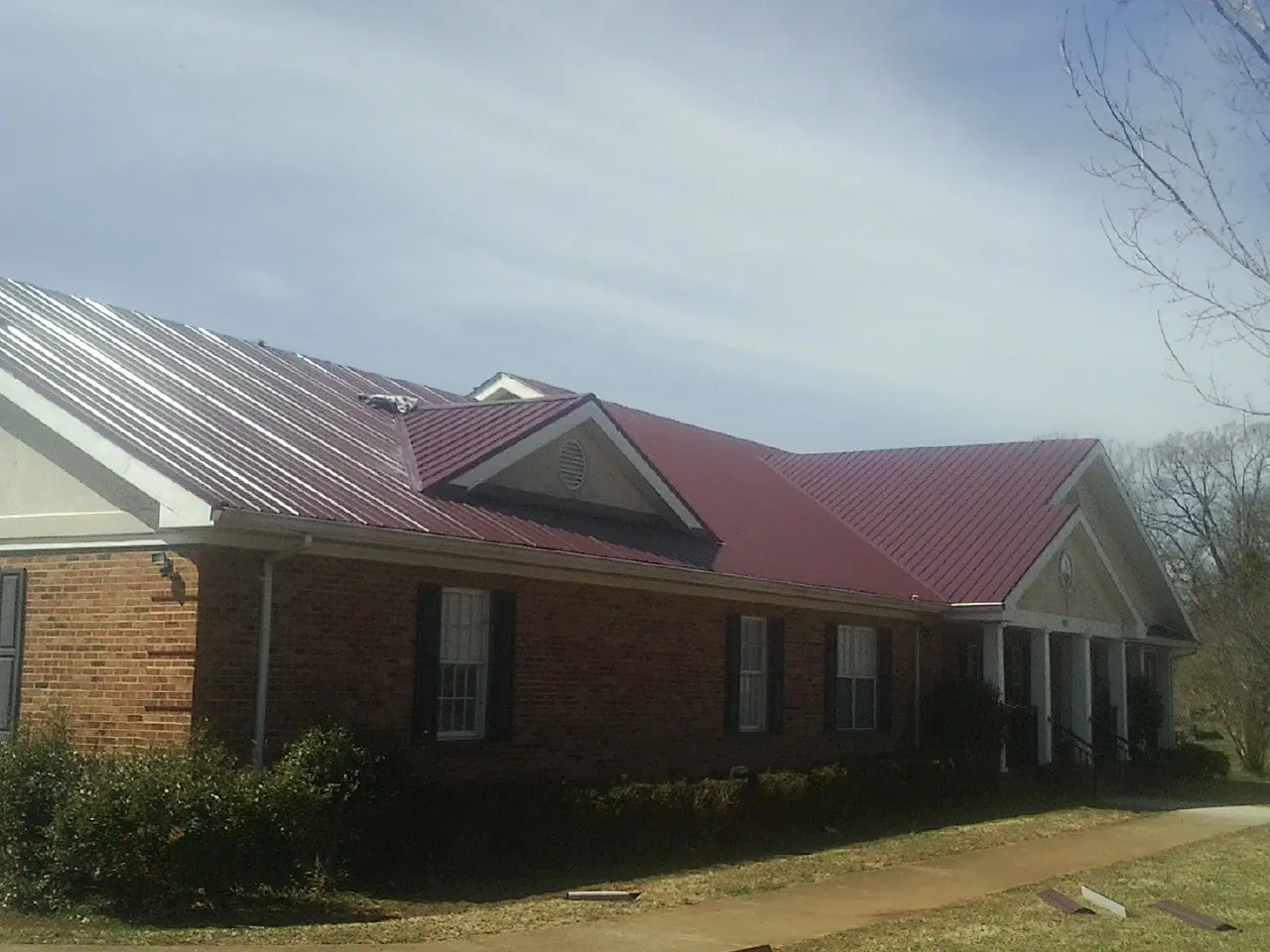 Red metal roof with gabled entries on a long brick building, from a Hail Damage Roof Repair job in Green Isle