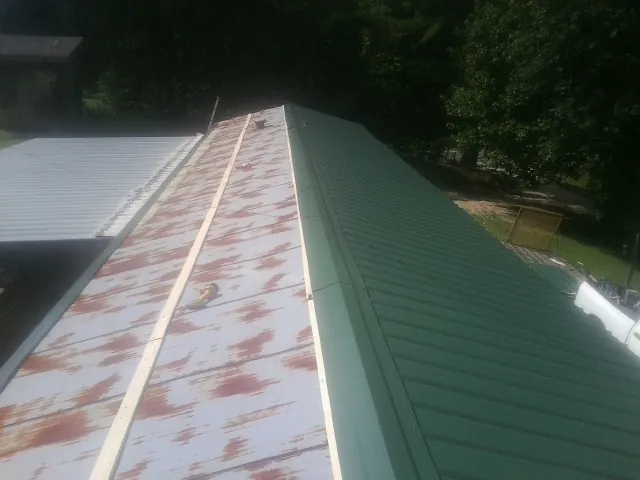 Old rusted panels beside newly installed green metal roofing — Wind Damage Roof Repair by Roofing Brothers in Green Isle