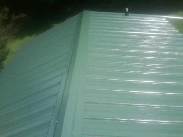 New green metal panels meeting at the ridge of a roof — Flat Roof Repair work by our crew in Green Isle