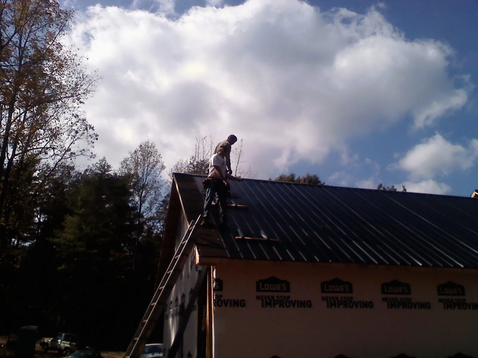 Roofer fastening dark metal panels high against a cloudy sky, from a Roof Inspection job in Green Isle