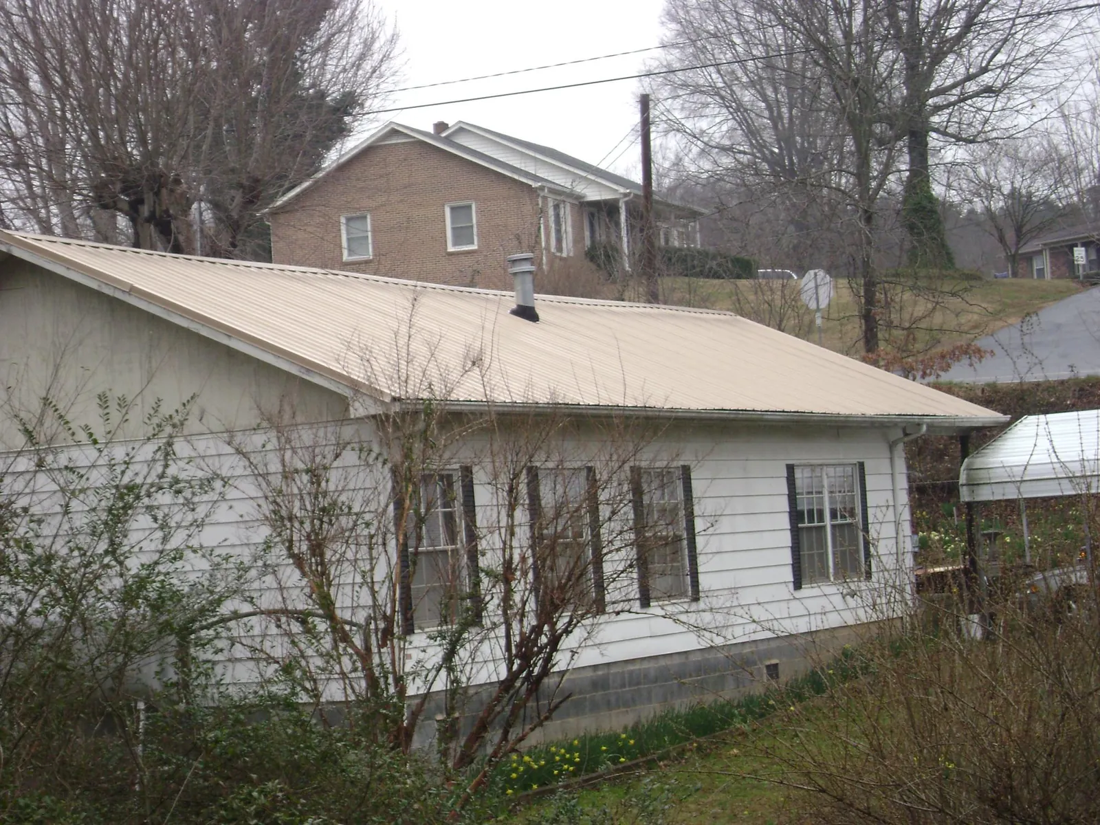 Tan metal roof on a white sided house set into a hillside — Commercial Roofing by Roofing Brothers in Green Isle