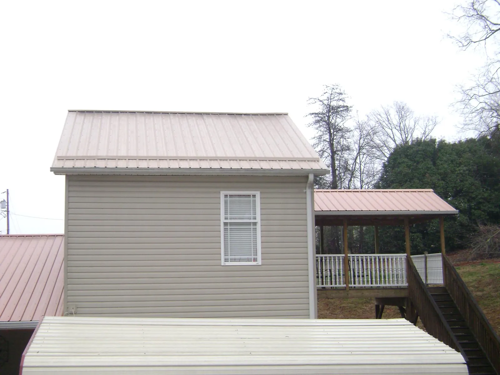 Tan metal roofs on a two story addition and attached porch, from a Roof Replacement job in Green Isle
